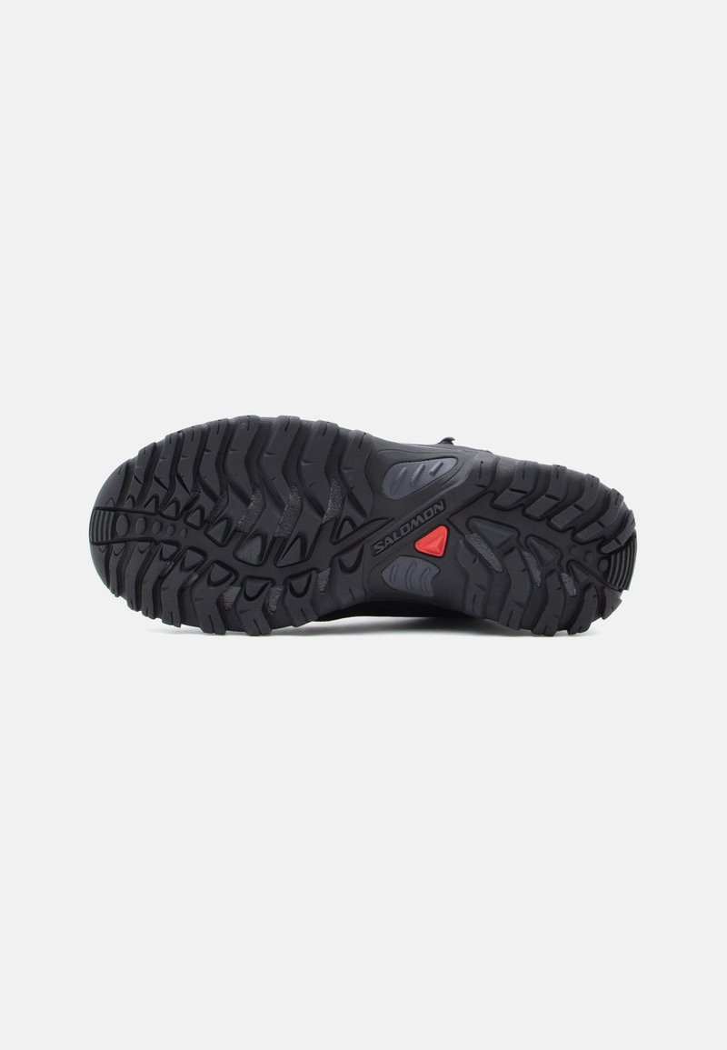 Schwarze Sneaker-Sohle mit einem robusten Profil, einem roten Akzent und dem Markenlogo. Das Material scheint langlebig zu sein und weist unterschiedliche Texturen für besseren Grip auf.