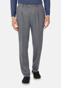 Sive volnene hlače s ravnim krojem, ki vključujejo dvojne plitvice, gumbe za zapiranje in stranske žepe. Utežene so z mornarsko modrimi čevlji.