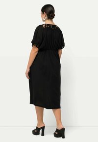 Vestido negro hasta la rodilla con mangas cortas, detalles de encaje en el escote, cintura elástica y combinado con tacones de plataforma negros.