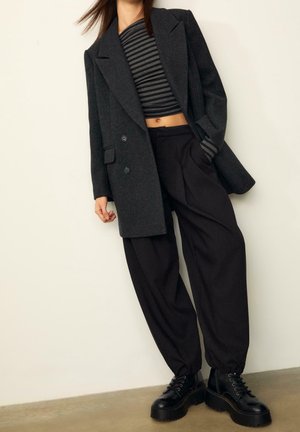 Osoba nosząca ciemnoszary oversize’owy blezer, czarno-szary paskowany crop top, szerokie czarne spodnie oraz czarne platformowe botki na sznurowadła.