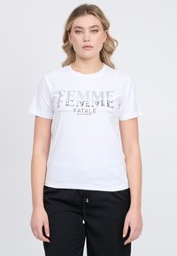 Hvid bomulds t-shirt med "FEMME FATALE" trykt i sølv, med klassisk rund hals og korte ærmer, parret med sorte bukser.