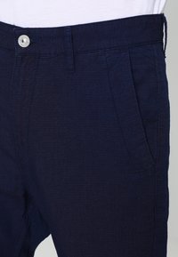 Donkerblauwe linnen broek met een textuur, voorzien van een voorkeuze en een metalen knoopsluiting bij de taille.