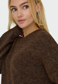 Brun strikket sweater med en blød tekstur, der har en bred udskæring og en afslappet pasform. Stof er i en subtil meleret mønster.