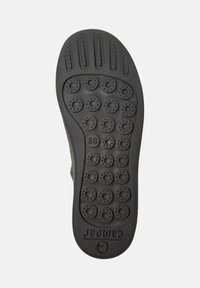 Suela de zapato negra con patrones texturizados y una marca de tamaño '38', que presenta indentaciones redondas para el agarre y la flexibilidad.