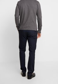 Chemise à manches longues gris foncé associée à un pantalon de costume bleu marine. Le pantalon a une texture lisse, tandis que la chemise présente un col rond et des manches ajustées.