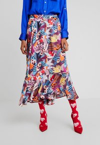Kolorowa, drukowana spódnica midi z falbaną na dole, z motywem kwiatowym w odcieniach niebieskiego, czerwonego, różowego i pomarańczowego. Do tego czerwone skarpetki z wzorem serc.