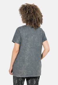 T-shirt grigia con una texture usurata e sbiadita, maniche corte e scollatura rotonda. Indossata con leggings neri a fantasia.