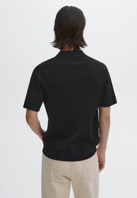Musta ribbine lyhythihainen neule klassisella kauluksella, jossa on slim fit -design ja hienovarainen tekstuuri, yhdistettynä vaaleisiin housuihin.