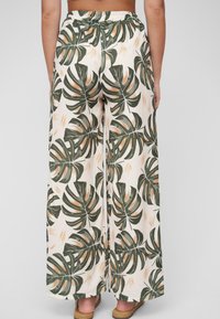 Pantalones de pierna ancha hechos de tela ligera con un estampado de hojas tropicales en verde y naranja sobre un fondo crema. Cintura elástica.