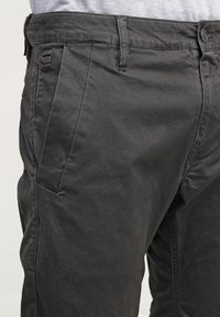 Svarta chinos i bomull med en slät textur, utrustade med knappstängning, sidfickor och en liten etikett vid midjebandet.