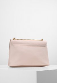 Růžová syntetická kabelka s pevnou strukturou, zlatým řetízkovým popruhem a hladkým, texturovaným povrchem. Má klopu uzavírající horní část.