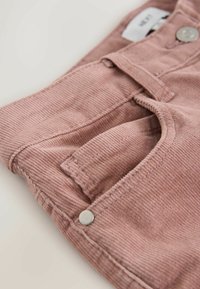 Pantaloni din catifea roz, cu o finisare texturată, având un buzunar frontal și un nasture metalic. Materialul este moale, cu dungi verticale fine.