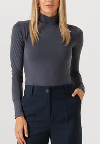 Grijze lange mouw turtleneck top gemaakt van glad, aansluitend materiaal; gecombineerd met donkerblauwe broek met een knoopdetail bij de taille.