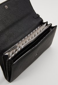 Portafoglio in pelle nera texturizzata aperto, che mostra più scomparti con fodera interna a righe grigio chiaro e bianco e tasca con zip.