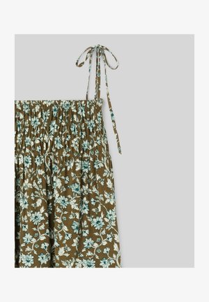 Tissu marron à motif floral blanc et vert, haut élastique froncé, et fines bretelles nouées aux épaules sur un fond gris.