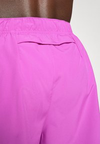 Helle pinke Shorts mit glatter Oberfläche, elastischem Bund und einer Gesäßtasche. Der Stoff wirkt leicht und atmungsaktiv.