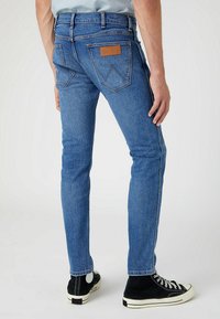 Tajta blå denimjeans med medelhög midja, sömnadsdetaljer, två bakfickor och en läderlogg. I kombination med svarta sneakers.