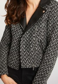 Svart och vit hounds-tooth-mönstrad jacka med läderdetaljer, kort design, dragkedjefickor och slagkrage.