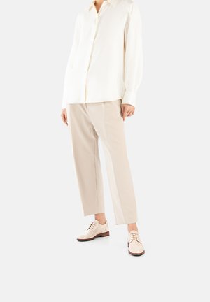 Camicia button-up in seta crema, pantaloni beige su misura e scarpe stringate chiari con finitura liscia e suole in legno.