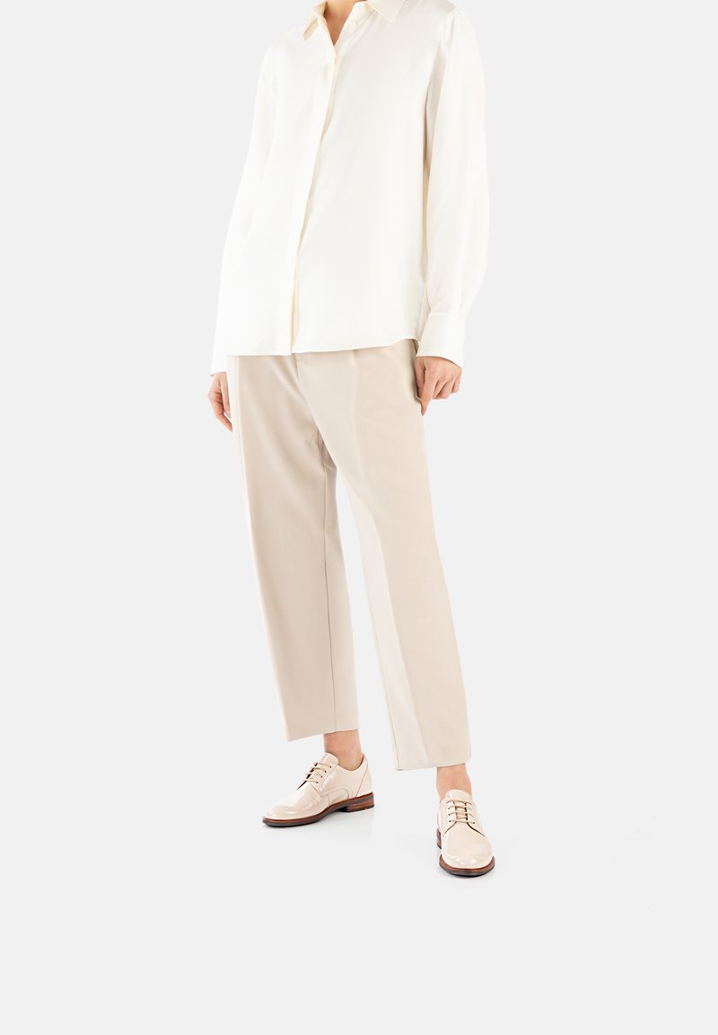 Camicia button-up in seta crema, pantaloni beige su misura e scarpe stringate chiari con finitura liscia e suole in legno.