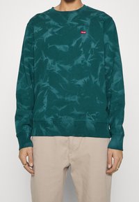 Teal sweatshirt met een tie-dye patroon, ronde hals, geribbeld bij de mouwen en onderkant, met een klein rood Levi's logo op de borst.