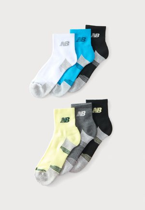 Seks par New Balance ankelsokker i hvid, blå, sort, gul, grå og sort med grå tæer og hæle, arrangeret på en lys baggrund.