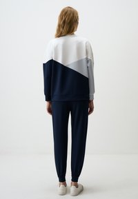 Sweatshirt- en joggingbroekset in marineblauw en lichtgrijs met een kleurblokontwerp. Losse pasvorm, geribde boorden en zachte stoftextuur. Witte sneakers.