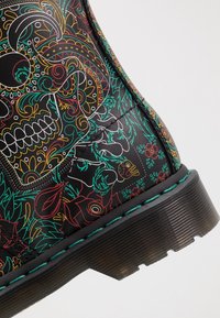 Botas de cuero negro con vibrantes e intrincados patrones florales y de calaveras en verde, rojo y amarillo, con un acabado texturizado y una suela gruesa.