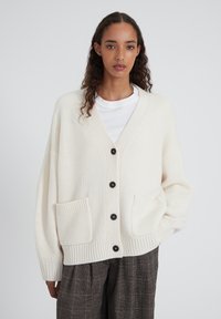 Cardigan en maille crème surdimensionné avec col en V, six boutons noirs, deux poches avant, et ourlet et poignets côtelés.