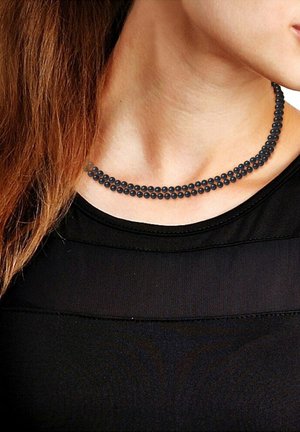 Collier de perles noires avec trois rangées de perles de taille uniforme, présentant une texture lisse et une forme ronde, reposant sur un haut noir.