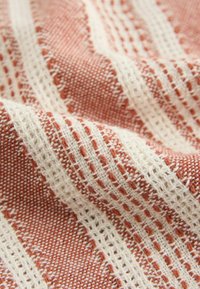 Woven fabric featuring alternating patterns of rust and cream stripes with textured, open weave sections and tightly knit areas.