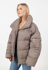 Giubbotto imbottito di colore taupe con colletto alto, chiusura con zip e polsini elasticizzati; presenta una tasca utilitaria sulla manica sinistra.