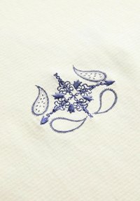 Cremefarvet stof med intrikate marineblå paisley- og blomsterbroderinger samt tekstureret baggrund.