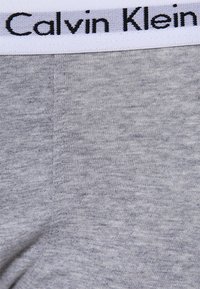 Sivé bavlnené prádlo s hladkou textúrou, so bielym pásom, na ktorom je čierne značenie "Calvin Klein".