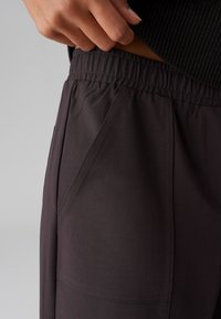 Pantaloni sportivi grigio scuro con vita elastica, tasche laterali e una texture del tessuto liscia. Presentano dettagli di cucitura angolare.