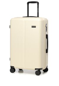 Valise rigide en crème avec un design texturé à nervures, roues et poignée noires. Elle est dotée d'une fermeture éclair et d'un petit logo à l'avant.
