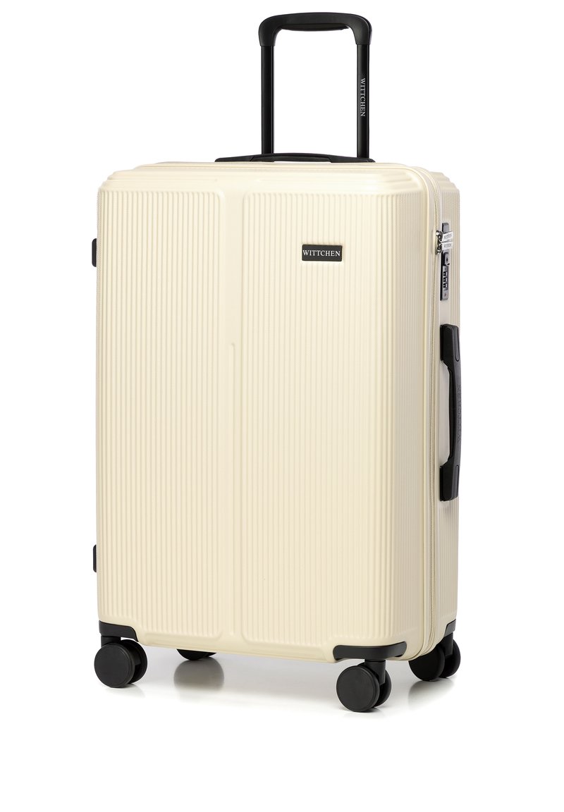Valise rigide en crème avec un design texturé à nervures, roues et poignée noires. Elle est dotée d'une fermeture éclair et d'un petit logo à l'avant.