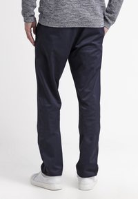 Granatowe spodnie o gładkiej fakturze, prostym kroju i bocznych kieszeniach. Noszone z białymi trampkami i szarym, o fakturowanej strukturze swetrem.