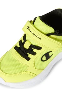 Gelbe Netzsportschuhe mit schwarzen Akzenten, ausgestattet mit einem Klettverschluss, schwarzen Schnürsenkeln und einer strukturierten Sohle. Logo an der Seite sichtbar.