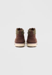 Braune Wildleder-Stiefeletten mit olivgrünen Textilakzenten, einem gepolsterten Kragen und einer kontrastierenden weißen Sohle mit roten und schwarzen Streifen.