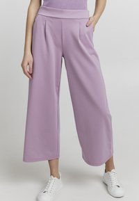 Liliowe spodnie o szerokich nogawkach wykonane z miękkiego materiału o gładkiej fakturze, z wysokim stanem i plisami z przodu. W połączeniu z białymi trampkami.