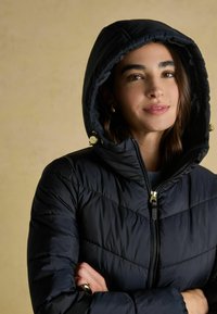 Granatowa kurtka puchowa z kapturem, z zamkiem błyskawicznym, złotymi detalami oraz pikowanym teksturem.