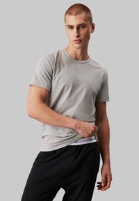 Gray short-sleeve t-shirt with a rounded neckline, paired with black pants featuring Calvin Klein branding on the waistband.