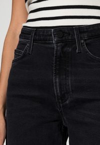 Czarne dżinsy z denimu o wysokim stanie, klasycznym fasonie z pięcioma kieszeniami oraz zapięciu na przód na guziki, z subtelnym teksturowanym wykończeniem.