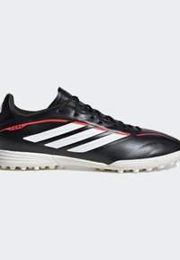 Chaussure de football Adidas Copa noir et blanc avec des accents rouges, des lacets rouges et de petits crampons en caoutchouc sur la semelle pour jouer sur gazon synthétique.