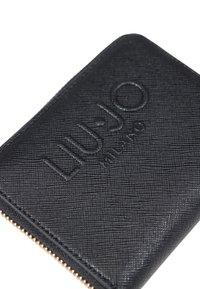 Portafoglio nero con finitura testurizzata, logo impresso e dettaglio della cerniera dorata lungo il bordo. Forma quadrata senza motivi visibili.