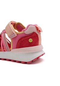 Zapatilla deportiva ajustable en rosa y rojo, con materiales de malla y gamuza, suela de goma moldeada y detalle del logo en el lateral.