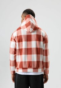 Flanellen hoodie met een rood-wit geruit patroon, zachte textuur, kangoeroezak en een capuchon met trekkoord. Voorzien van geribbelde manchetten en zoom.
