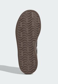 Crni potplat tenisica s valovitom teksturom u tamnosmeđoj boji, s Adidas logom na peti.