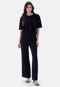 Marineblaues, mit Pailletten besetztes Crop-Top mit kurzen Ärmeln, kombiniert mit hochgeschlossenen schwarzen Hosen und schwarzen Riemchensandalen, das eine schlanke Passform bietet.